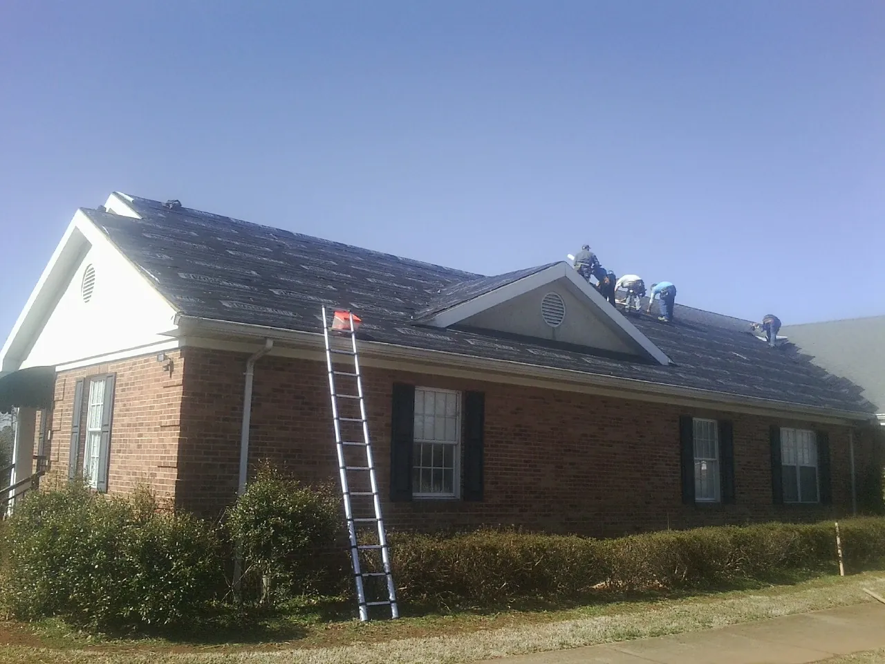 Crew tearing shingles off a brick ranch roof with a ladder set — Metal Roof Repair work by our crew in Waldo